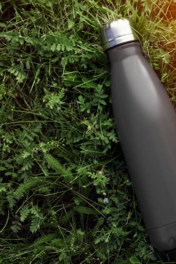Paslanmaz termos su şişesi, mat siyah renk. Güneş ışığı etkisi yeşil çim zemin üzerine izole mockup
