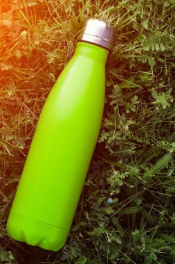 Paslanmaz termos su şişesi, mat açık yeşil renk. Güneş ışığı etkisi yeşil çim zemin üzerine izole mockup