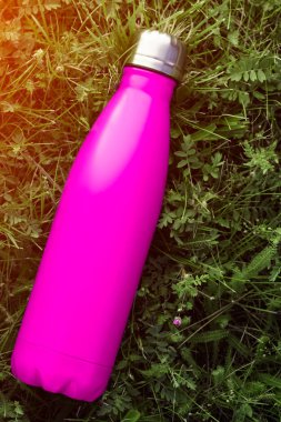 Paslanmaz termos su şişesi, mat pembe renk. Güneş ışığı etkisi yeşil çim zemin üzerine izole mockup