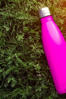 Paslanmaz termos su şişesi, mat pembe renk. Güneş ışığı etkisi yeşil çim zemin üzerine izole mockup