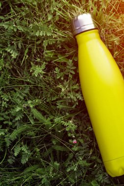 Paslanmaz termos su şişesi, mat açık sarı, limon renk. Güneş ışığı etkisi yeşil çim zemin üzerine izole mockup