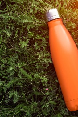 Paslanmaz termos su şişesi, mat orangecolor. Güneş ışığı etkisi yeşil çim zemin üzerine izole mockup