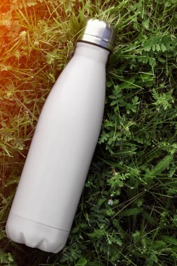 Paslanmaz termos su şişesi, beyaz renk. Güneş ışığı etkisi yeşil çim zemin üzerine izole mockup. Parlak alüminyum Vakum termo beyaz diş cep şişesi. Yatay fotoğraf