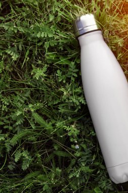 Paslanmaz termos su şişesi, beyaz renk. Güneş ışığı etkisi yeşil çim zemin üzerine izole mockup. Parlak alüminyum Vakum termo beyaz diş cep şişesi. Yatay fotoğraf