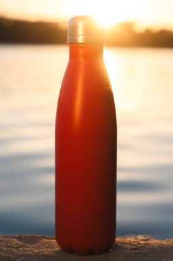 Paslanmaz kırmızı termo şişe su için. Günbatımı ve arka plan üzerinde su