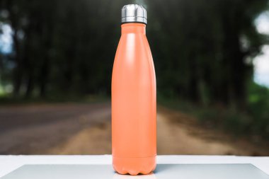 Paslanmaz termos su şişe beyaz masada açık. Turuncu renk