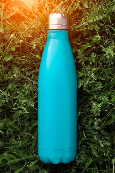 Paslanmaz termos su şişesi, açık mavi renk. Güneş ışığı etkisi yeşil çim zemin üzerine izole