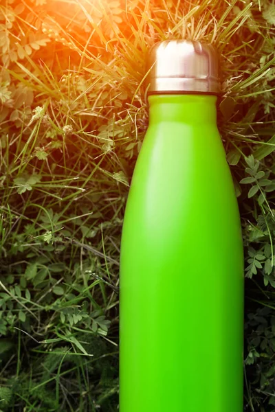 Stainless thermos water bottle, light green color. Mockup isolated on green grass background with sunlight effect. Glossy aluminum vacuum thermo tumbler flask