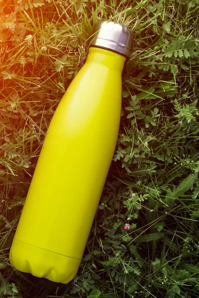 Paslanmaz termos su şişesi, mat açık sarı, limon renk. Güneş ışığı etkisi yeşil çim zemin üzerine izole mockup