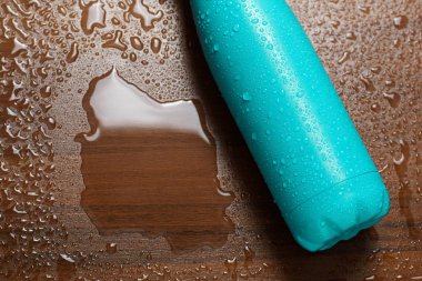 Paslanmaz çelik termos ahşap bir masaya izole şişe su ile püskürtülür. Açık mavi renk