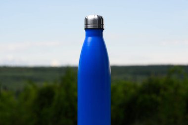 Termo Paslanmaz şişe su, çay veya kahve için. Gökyüzü ve orman arka plan üzerinde. Termos mat mavi renk