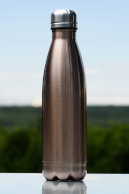 Termo Paslanmaz şişe su, çay veya kahve için. Gökyüzü ve orman arka plan üzerinde. Cam masanın üzerinde. Termos maro renk