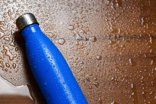 Stainless steel thermos bottle isolated on a wooden table sprayed with water.