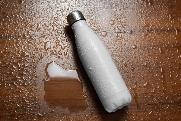 Stainless steel thermos bottle isolated on a wooden table sprayed with water. White color