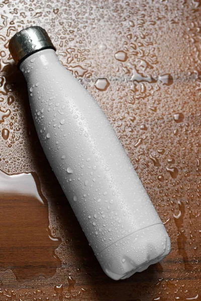 Stainless steel thermos bottle isolated on a wooden table sprayed with water. White color