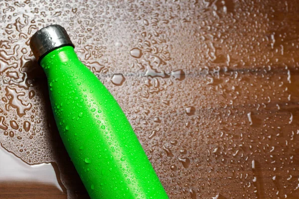 Stainless steel thermos bottle isolated on a wooden table sprayed with water. Light green color