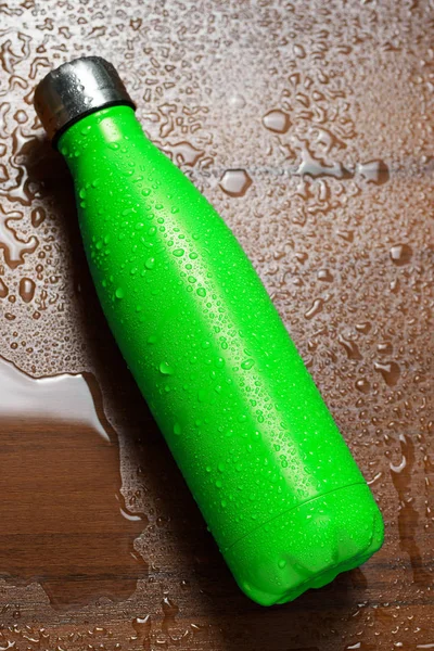 Stainless steel thermos bottle isolated on a wooden table sprayed with water. Light green color