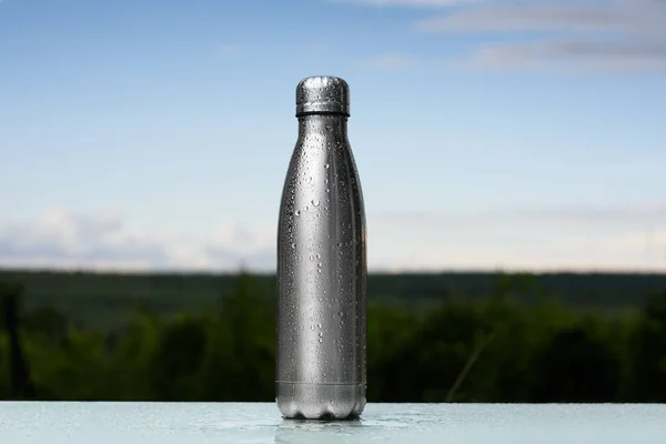 Thermos bottle sprayed with water. Against the sky background. Water tumbler..