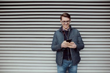 Genç bir çocuk bir smartphone cep telefonu ile internet tarama ve kulaklık ile müzik dinlemek