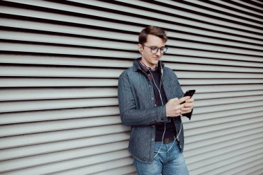 Genç bir çocuk bir smartphone cep telefonu ile internet tarama ve kulaklık ile müzik dinlemek