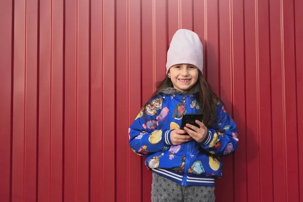 Šťastná Dívka Dítě Smartphonem Ruce Červeném Pozadí Ulici Oblečený Modré — Stock fotografie