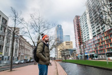 Sıcak giyinmiş genç bir adam, yağmurlu havalarda sabahları şehrin inceliyor. Rotterdam, Hollanda.