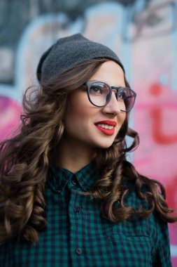 Şirin hippi kız gülümsüyor. O kırmızı dudaklar ve kıvırcık saçları vardır. Görüş için gözlük takıyor..