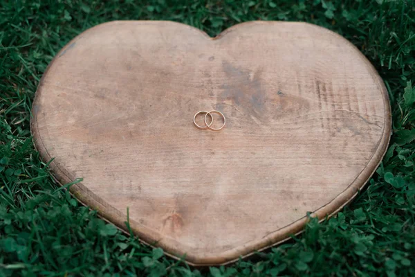 Wedding rings on a heart-shaped wood placed on the grass