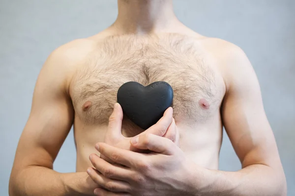 Portrait of black heart in man hands, on body torso background