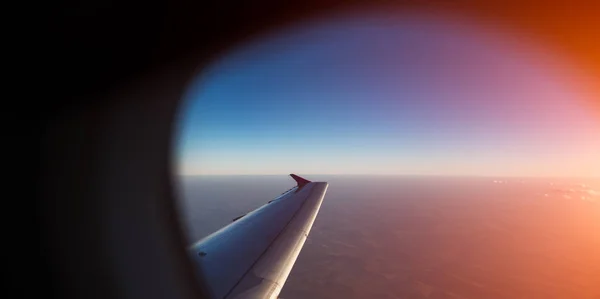 Blick auf Flugzeugflügel durch Fenster. bei Sonnenuntergang über der Erde fliegen. — Stockfoto