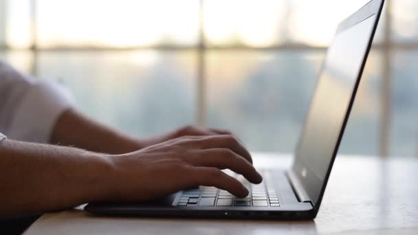 Крупный план, руки человека, печатающего на клавиатуре ноутбука поверх спинки окна . — стоковое видео