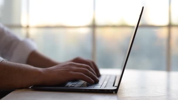 Close-up, handen van de mens te typen op het toetsenbord van de laptop over backgroudn van venster. — Stockvideo