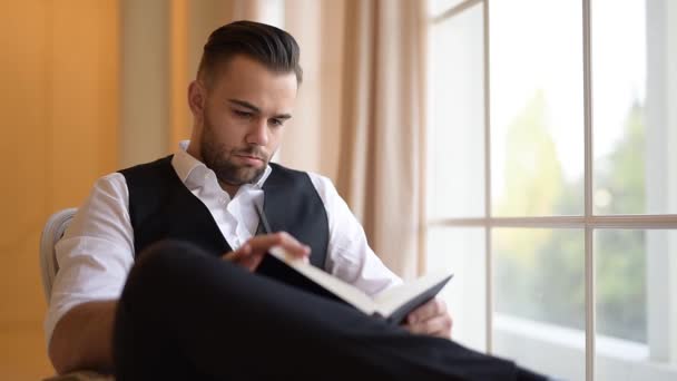 Empresario sentado en un sillón y hojeando un libro . — Vídeos de Stock