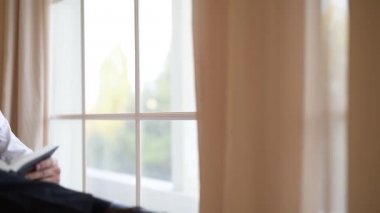 Koltukta oturan genç bir adam ve bir kitap ove arka plan penceresinin döndürür.