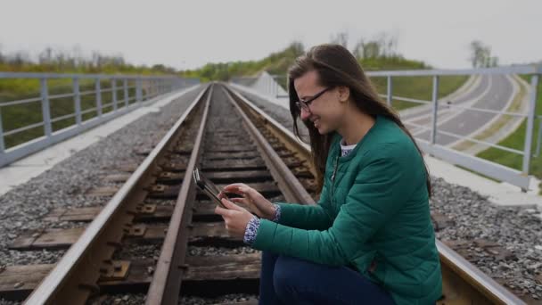 タブレットを使用して、鉄道で立っている笑顔若い女の子。メガネを着用し、緑の服を着て. — ストック動画