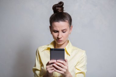 Genç kız video oyunları smartphone, beyaz arka plan üzerinde oynarken portresi. Sarı gömlek giymiş
