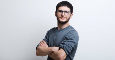 Kendine güvenen adam beyaz arka plan üzerinde gülümseyen genç portresi. Gözlük ve gri kazak giyiyor.