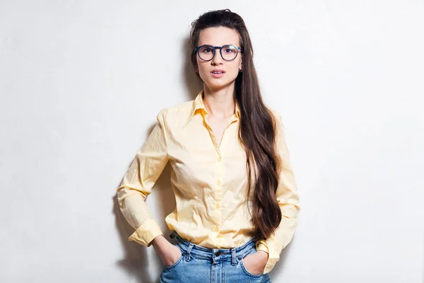 Young surprised girl over white studio background. Wearing blue glasses, jeans and yellow shirt
