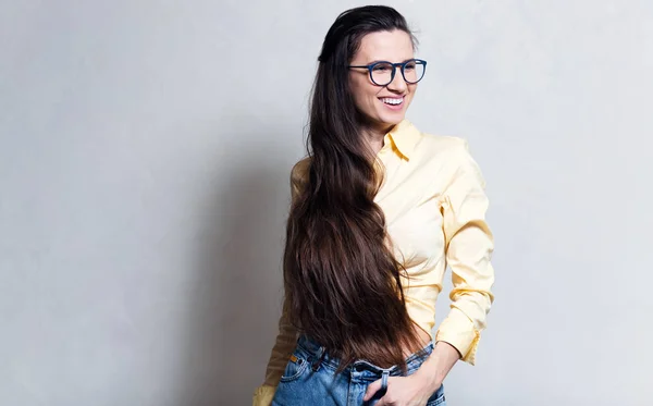 年轻微笑的女孩的肖像 戴蓝色眼镜 牛仔裤和黄色衬衫 — 图库照片