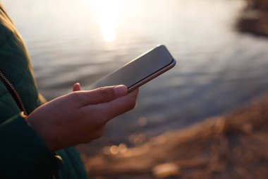 Gün batımı arka plan üzerinde eldeki akıllı telefon tutma.