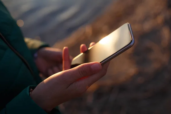 Trzymanie smartfona w dłoni na tle zachodu słońca. — Zdjęcie stockowe