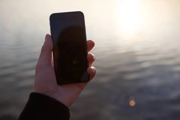 Hålla smartphone i handen över solnedgången bakgrund. — Stockfoto