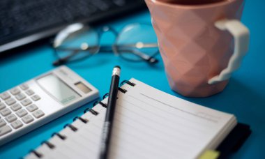 Hesap makinesi ve klavye ile mavi ofis masası, Not defteri boş, çay ve gözlük kupa