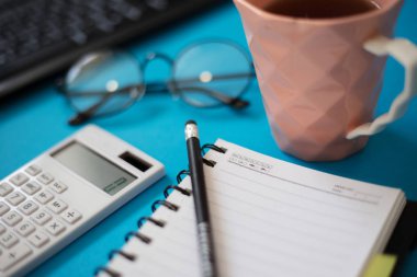 Hesap makinesi ve klavye ile mavi ofis masası, Not defteri boş, çay ve gözlük kupa.