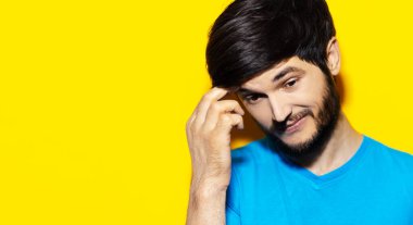 Stüdyo yakın plan portresi. Şüpheli duygular hisseden, mavi tişört giyen, el ele tutuşan, fotokopi alanı olan sarı bir arka plan..