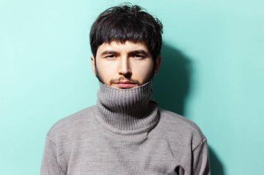 Aqua menthe renginin arka planında süveter giyen genç adamın stüdyo portresi.