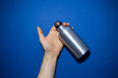 Yeniden kullanılabilir alüminyum termo su şişesini tutan erkek eli yakın plan. Renkli hayalet maviye izole edilmiş..