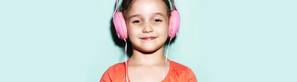 ピンクのヘッドフォンで音楽を聞いて喜びの小さな十代の少女のパノラマの肖像画 サンゴのシャツを着て シアンの背景 アクアメンソールの色 — ストック写真