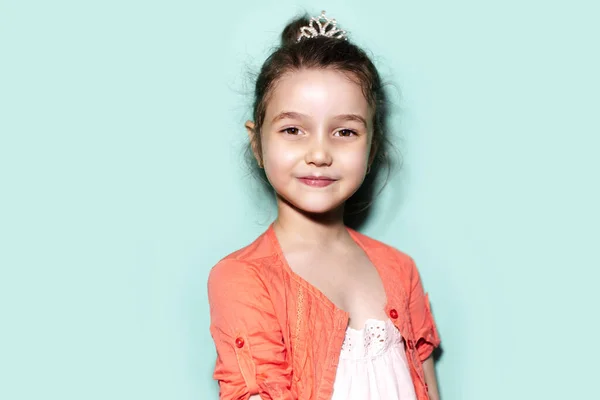 アクアメンソールの色を背景に明るい子供の女の子のスタジオの肖像画 サンゴのシャツとプリンセスクラウンを身に着けて — ストック写真