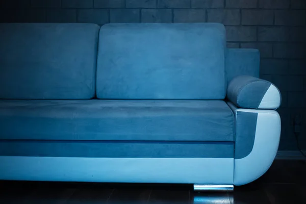 Close-up of part of blue sofa on the background of black brick wall.